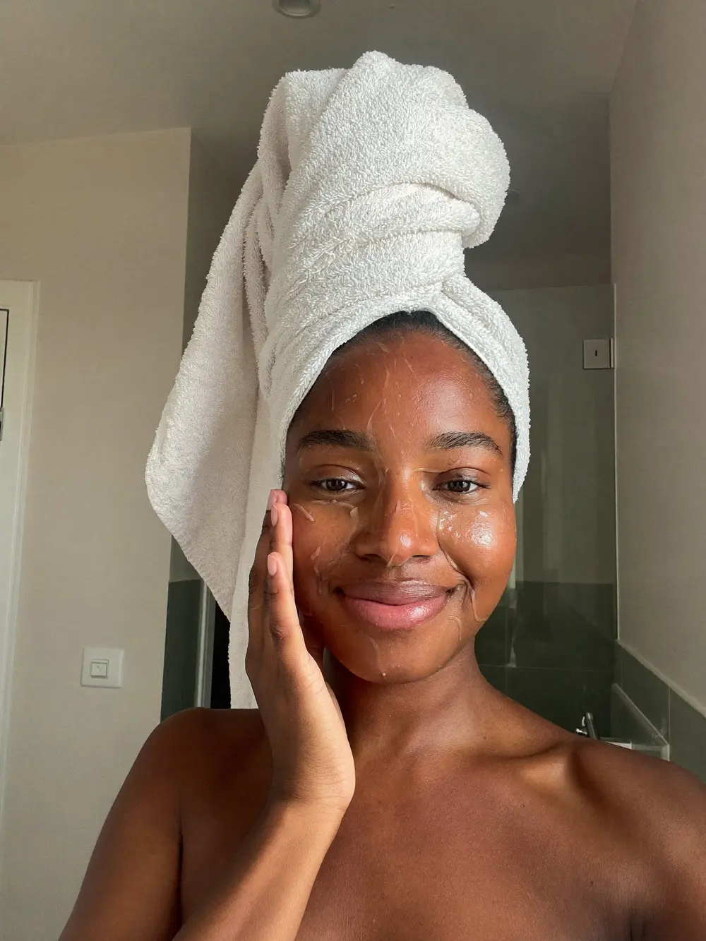 Mulher negra sorrindo com uma toalha na cabeça depois da rotina de skincare