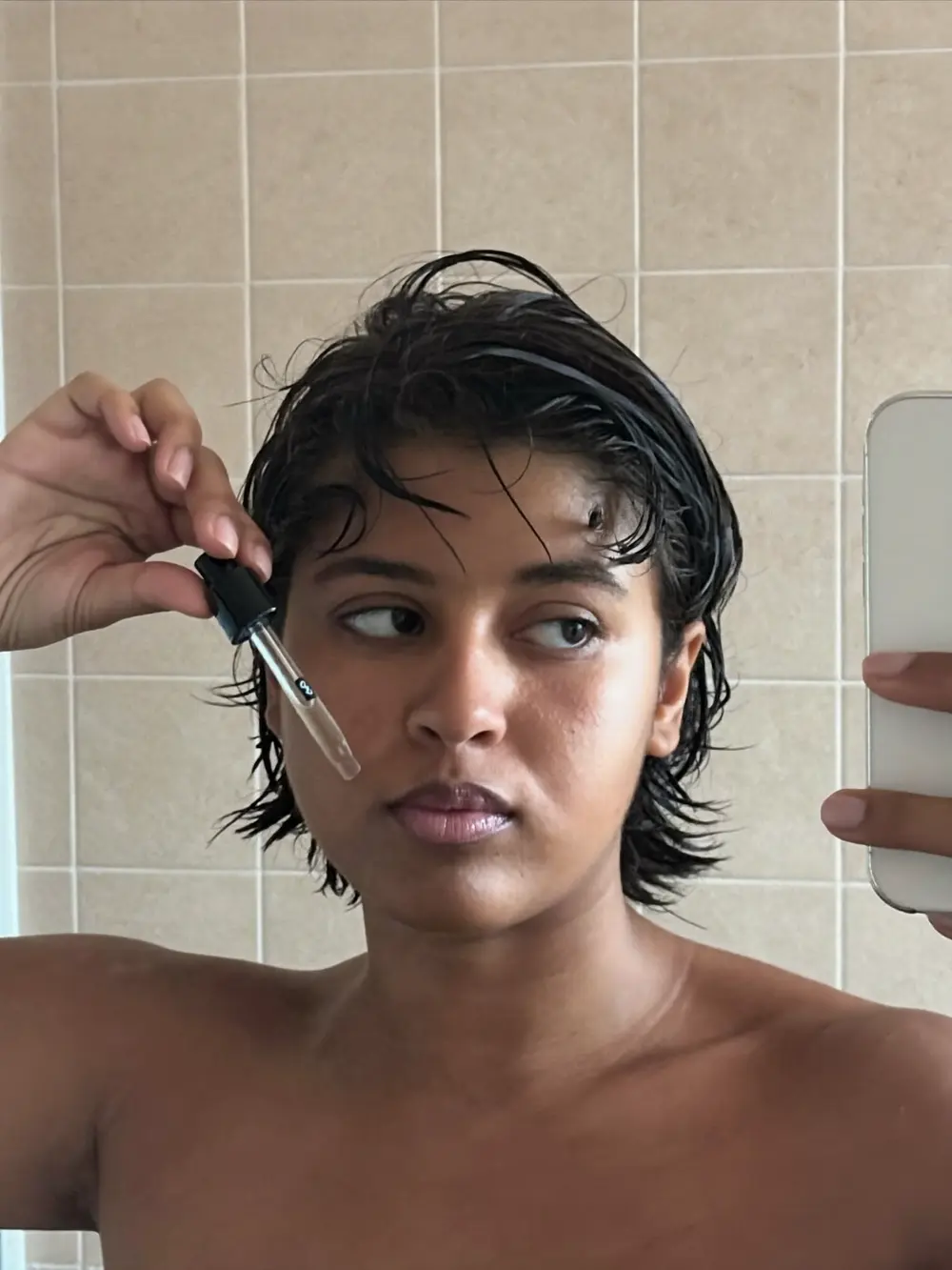 Selfie no espelho: jovem negra de cabelo curto aplicando sérum com conta-gotas